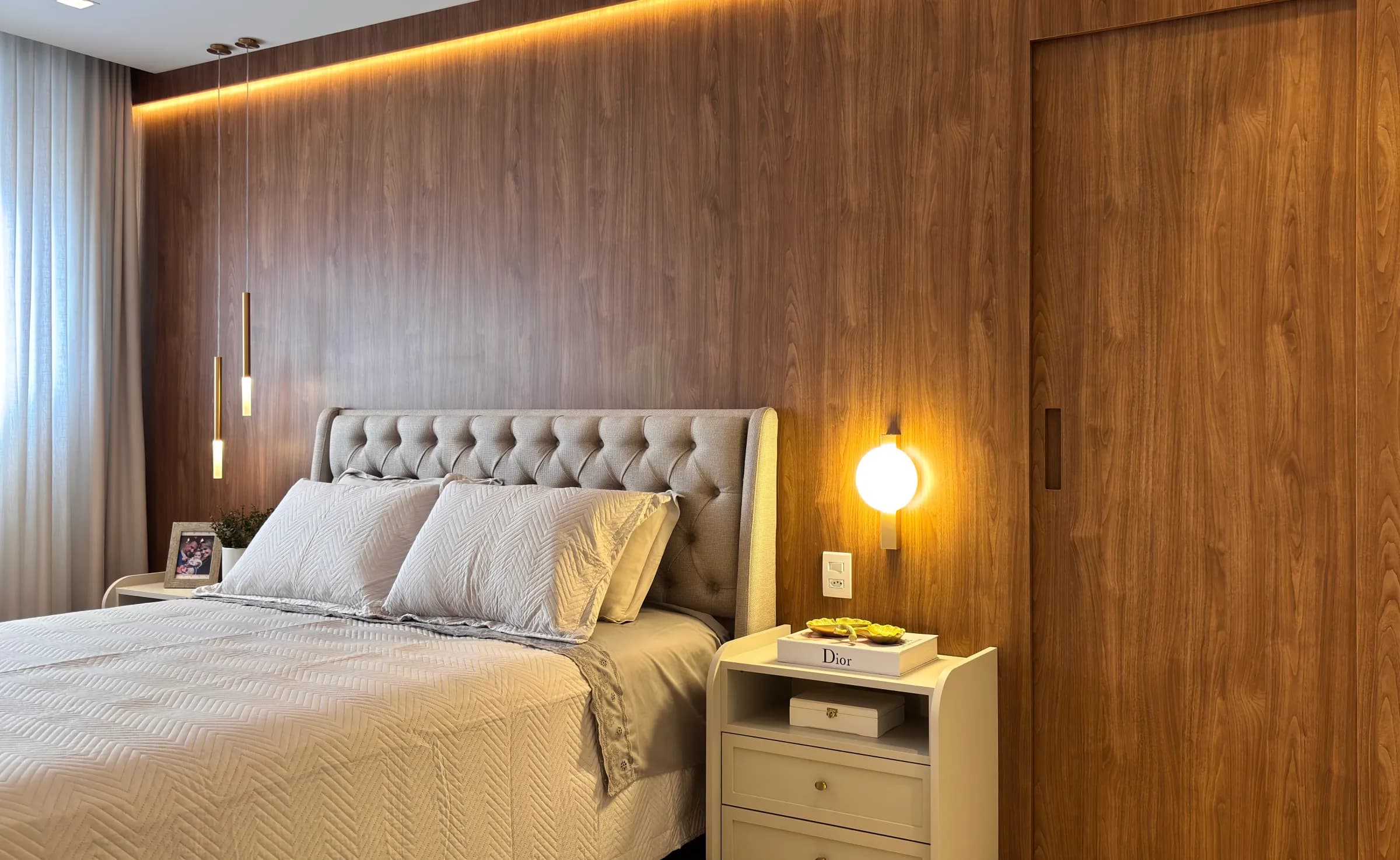 Suíte com painel amadeirado, iluminação embutida e marcenaria sob medida da Goulart Móveis.